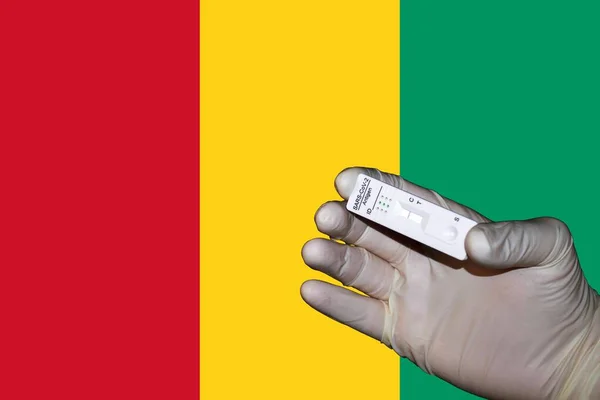 A hand showing a negative antigenic corona rapid test in front of a Flag of Guinea.