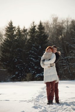 Mutlu çift Kış park orman arka plan üzerinde sarılmak.