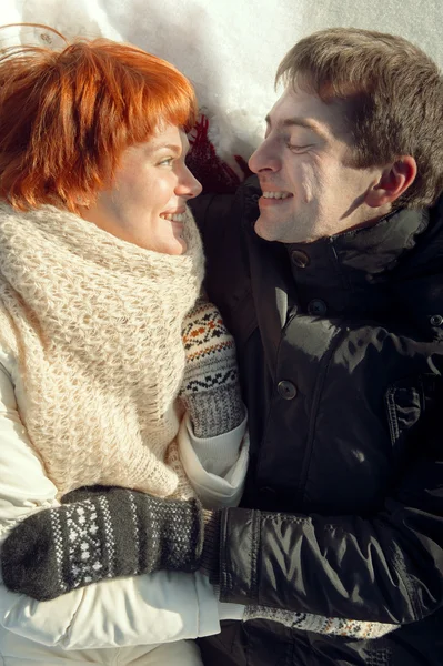 Feliz joven pareja sonriente yaciendo en la nieve y mirando a cada oth — Foto de Stock