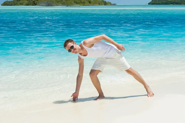 Mann spritzt Wasser aus dem Ozean an weißem Strand — Stockfoto