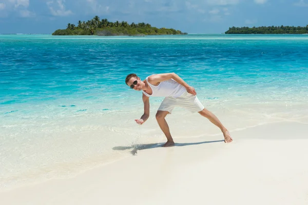 Чоловік бризкає воду океану на білому пляжі — стокове фото