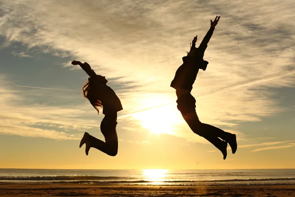 Couple or friends jumping on the beach at sunset — Stock Photo, Image