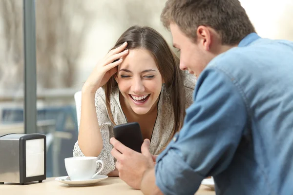 Pareja riendo viendo los medios en el teléfono inteligente — Foto de Stock