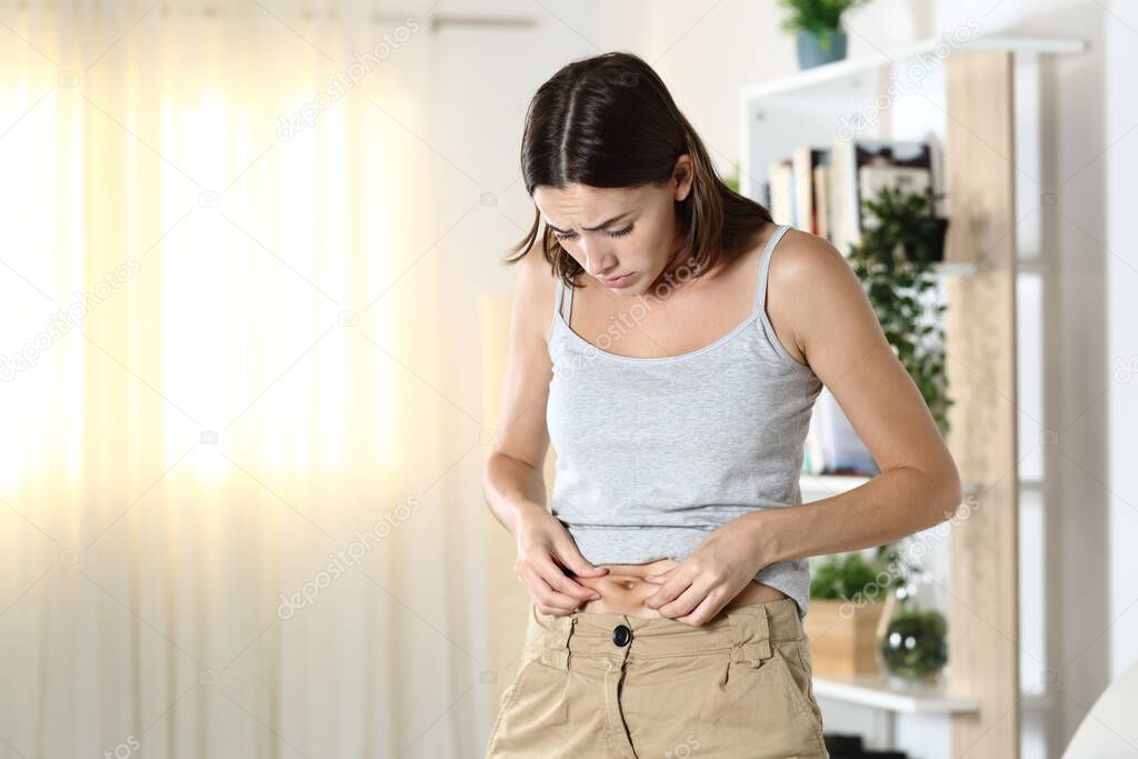 Woman worried about body fat touching her belly standing at home