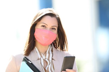 Maske takan mutlu girişimci Coronavirus salgınından kaçınıyor ve elinde akıllı bir telefonla sokakta sana bakıyor.