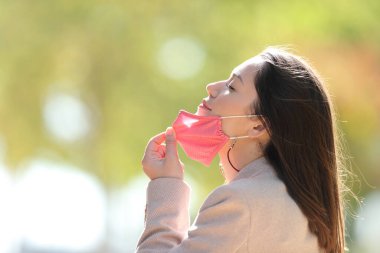 Coronavirus zamanlarında parkta maskesini çıkarıp temiz hava soluyan rahat bir kadının profili.
