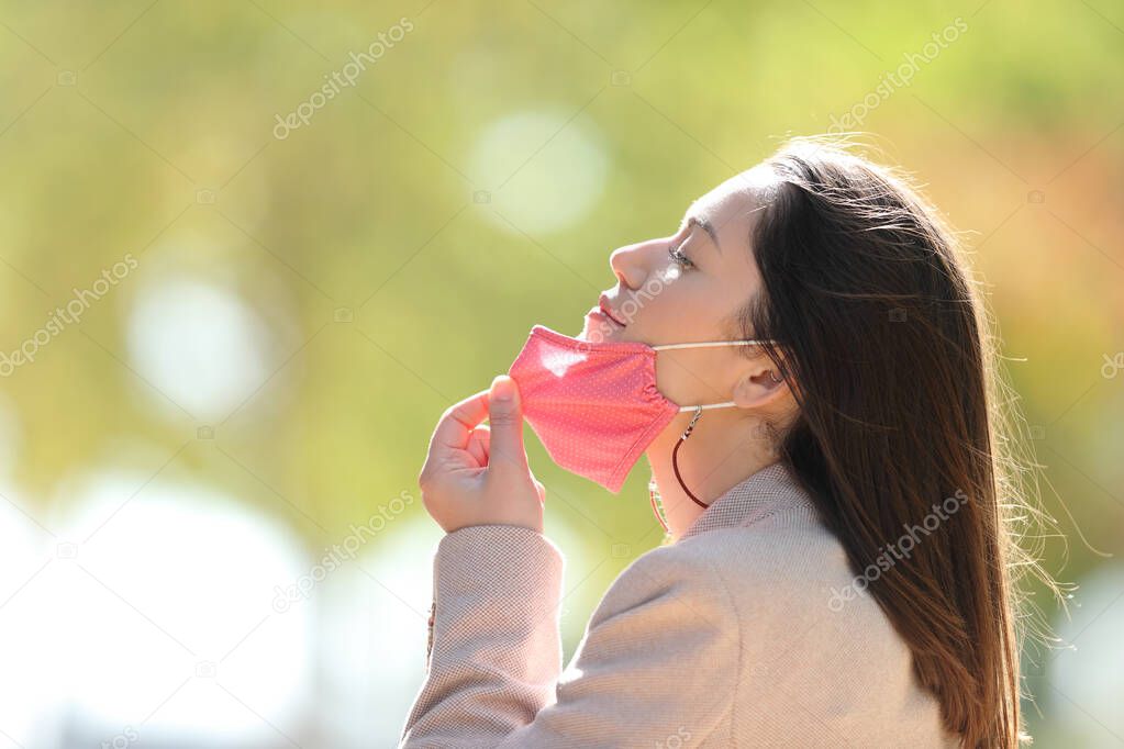 Profile of a relaxed woman taking off mask breathing fresh air in a park in coronavirus times