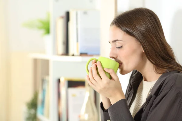 自宅のリビングルームに立つマグカップからコーヒーを飲む女性のプロフィール — ストック写真