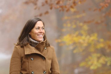 Happy adult lady contemplating views walking in a park in fall season clipart