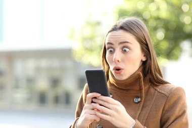 Şaşkın kadın, kışın sokakta cep telefonunu kontrol ediyor.