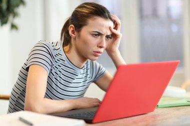 Endişeli kadın evdeki oturma odasında kırmızı laptopu kontrol ediyor.
