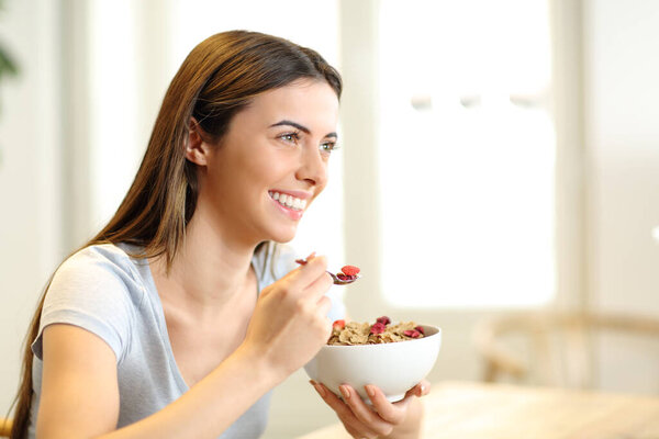 Happy woman eating cereals from bowl for breakfast in the living room at home