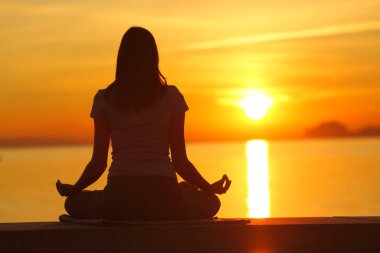 Sahilde gün batımında yoga yapan bir kadının arka plan portresi.