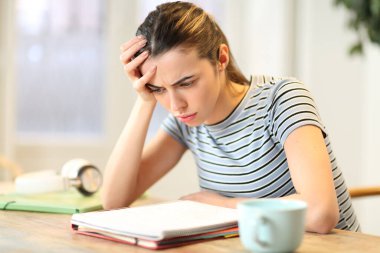 Hüsrana uğramış öğrenci evdeki not defterinde karmaşık ders okuma notları okuyor.