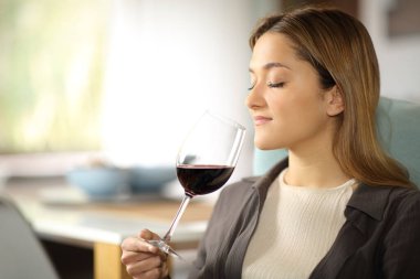 Ciddi bir kadın evdeki koltukta oturmuş bardaktan şarap kokusu alıyor.