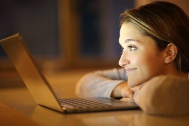 Memnuniyet duyulan bir kadının profili dizüstü bilgisayarı evde bir masada seyrediyor.