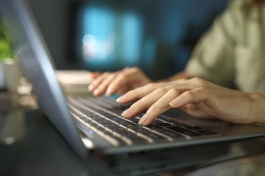 Gece evde dizüstü bilgisayarda yazı yazan bir kadının ellerini kapat.