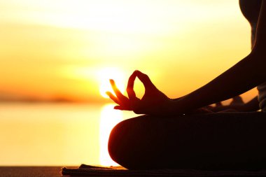 Sahilde gün batımında yoga egzersizi yapan kadın silueti.