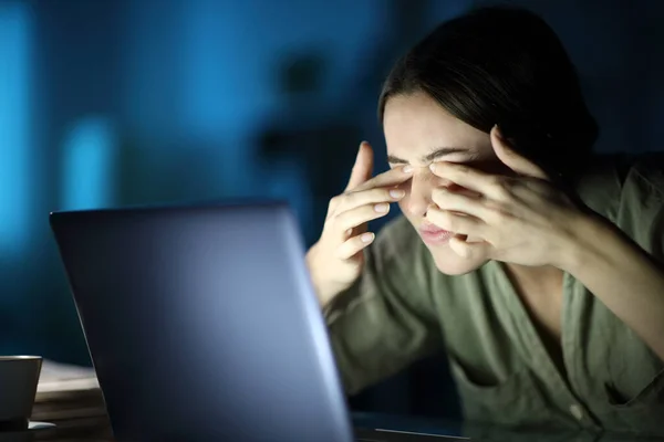 Fatigued woman with eyestrain scratching eyes using laptop late hours in the night at home