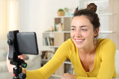 Mutlu kadın evdeki tripodla akıllı telefon içeriğini kontrol ediyor.