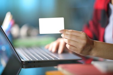 Gece evde dizüstü bilgisayar kullanarak boş kredi kartı gösteren bir öğrencinin fotoğrafını çek.