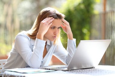 Ev terasında çalışırken dizüstü bilgisayardan kötü haberleri kontrol eden serbest çalışan endişeli biri.