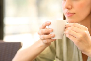 Güneşli bir günde, elinde kahve fincanı tutan bir kadının yakın çekimi.