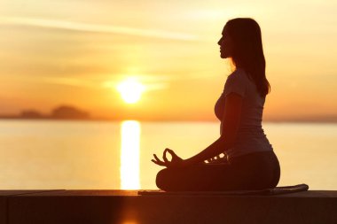 Sahilde gün batımında yoga yapan kadın siluetinin profil ışığı.