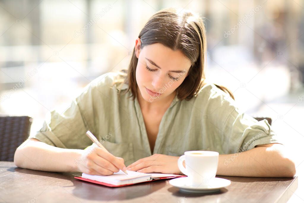 Front view portrait of a serious woman writing on agenda in a coffee shop