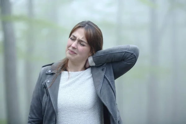 Woman suffering neck ache complaining alone in a foggy forest