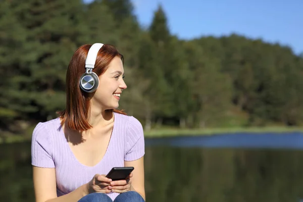 Happy Woman Listening Music Phone Wireless Headphones Looking Side Lake — Stock Photo, Image