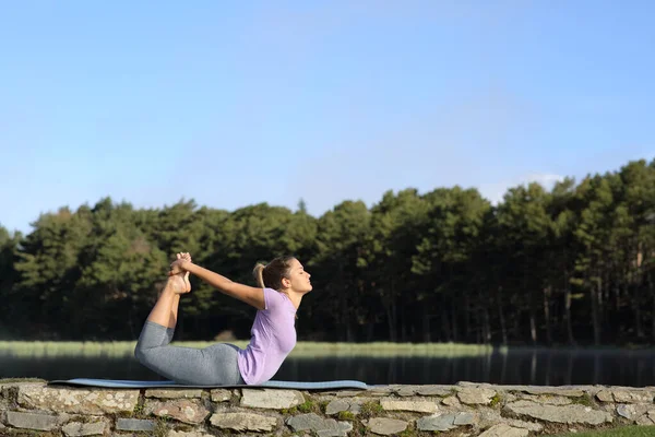 Profile of a woman doing yoga pose in the mountain beside a lake