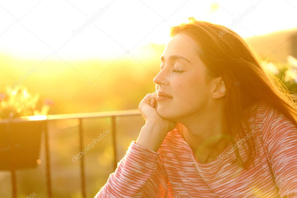 Relaxed woman feeling with closed eyes sitting in a balcony at sunset