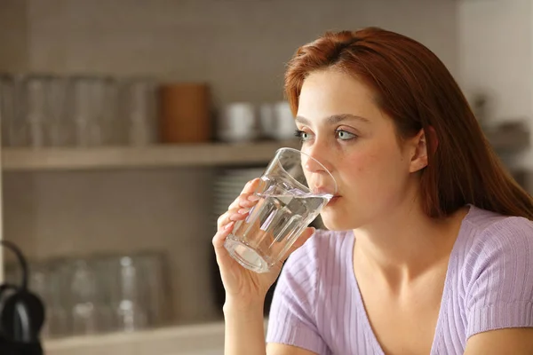 一个严肃的女人在厨房里用玻璃杯喝水 — 图库照片