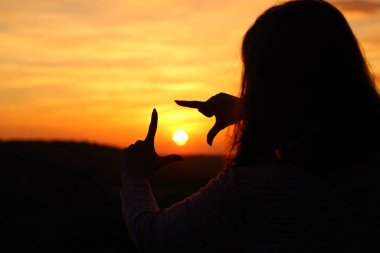 Bir kadının arka plan portresi. Gün batımında güneşi çerçeveleyen el silueti.