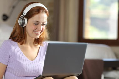 Yatak odasında video izlemek için dizüstü bilgisayar ve kulaklık kullanan mutlu kadın.