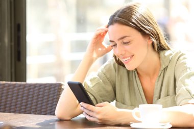Happy woman smiling checking smart phone content sitting in a coffee shop