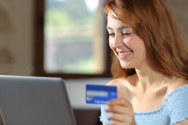 Happy woman using laptop paying with credit card in the bedroom at home
