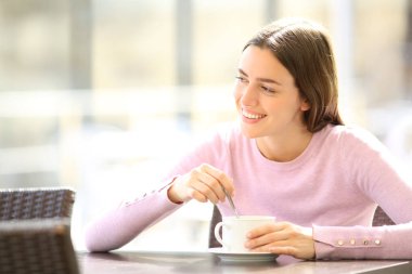 Happy woman stirring coffee sitting in a restaurant terrace