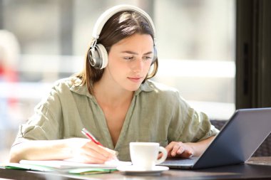 Bir kafede bilgisayar ve kulaklıkla konsantre öğrenci e-öğrenimi.