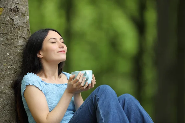 快乐的亚洲女人坐在森林里喝咖啡放松地呼吸新鲜空气 — 图库照片