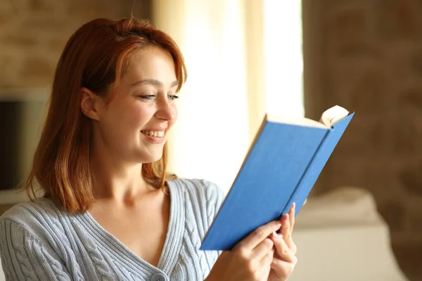 Happy Woman Reading Paper Book Seated Home Warm Light — Zdjęcie stockowe