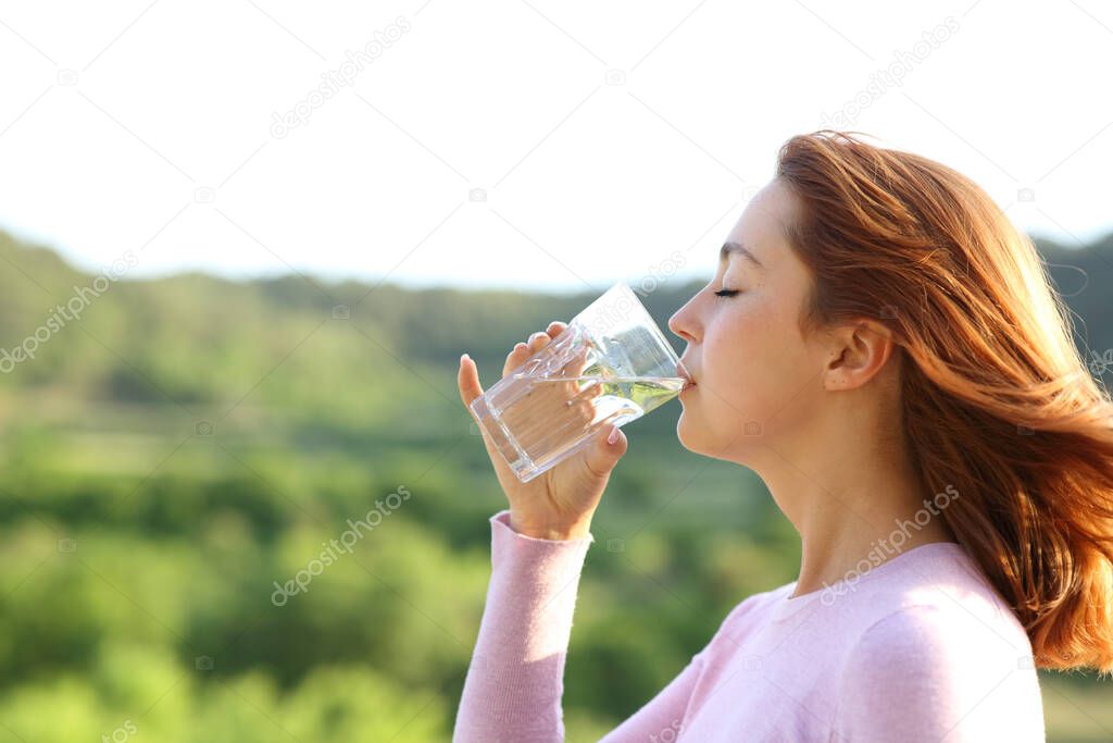 Profile of a woman drinking water from glass outdoor in nature