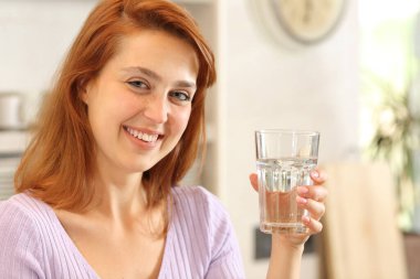 Happy female posing looking at camera holding a glass of water in the kitchen