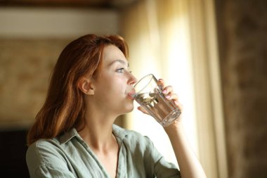 Woman drinking water from glass sitting at home or apartment