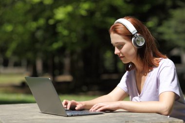 Profile of a woman with wireless headphones checking laptop in a park