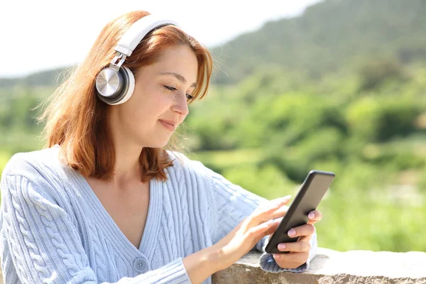バルコニーで携帯電話を使って音楽を聴く無線ヘッドフォンを装着した女性 — ストック写真