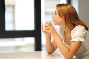 Evdeki pencereden kahve içen düşünceli kadın.