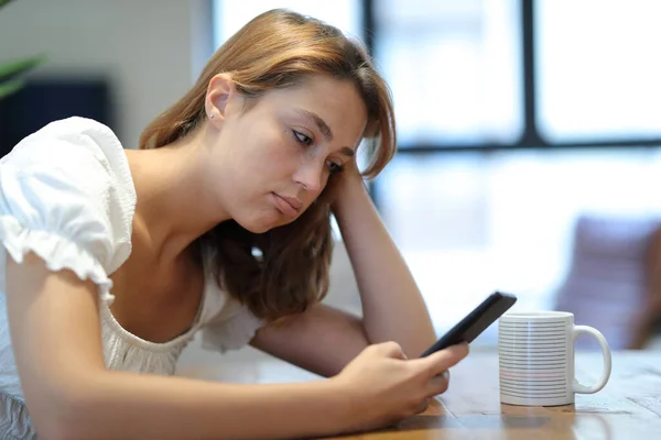 Frustrated and bored woman using smart phone checking content sitting at home
