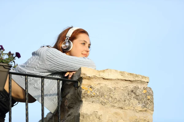 Ευτυχισμένη Γυναίκα Που Σκέφτεται Από Μπαλκόνι Ακούγοντας Μουσική Ακουστικά — Φωτογραφία Αρχείου